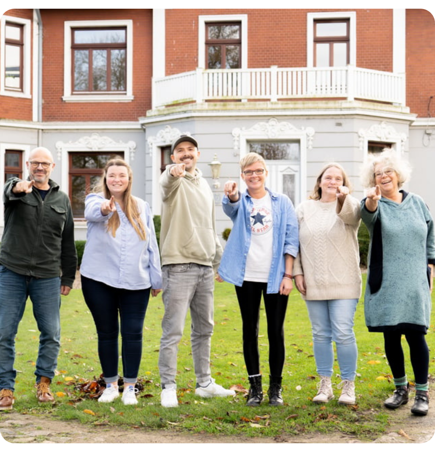 Mitarbeiter des Martinswerk stehen vor dem Hof in Bad Oldesloe und zeigen mit dem Finger auf den Betrachter des Fotos